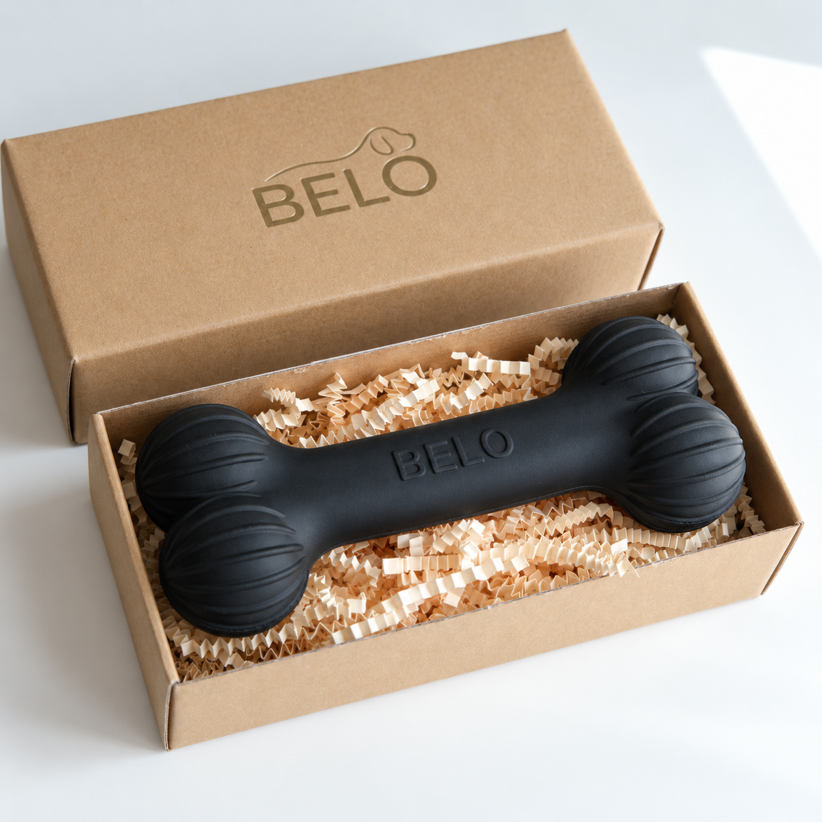 Midnight black BELO Aero Bone dog toy in an open cardboard box beside the branded lid